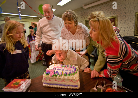 Unterstützt von Familie und Freunden, die einen hundertjährigen, die Kerzen auf ihrem Kuchen während ihrem 100. Geburtstag in einem Pflegeheim bläst Stockfoto