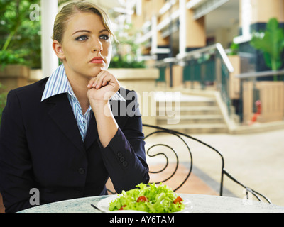 Junge Unternehmerinnen starrte etwas während ihr Mittagessen, eine Hand am Kinn Stockfoto