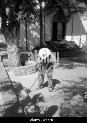 Ein andächtiger und ältere Hispanic Mann fegt den Hof des Chapilla de San Lorenzo, in San Lorenzo, New Mexico. Stockfoto