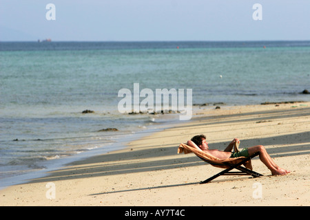 Mann im Liegestuhl entspannt am einsamen Strand mit Buch Ko Ngai Insel Thailand Stockfoto