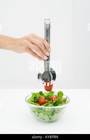 Frau Kommissionierung Tomate aus Salatschüssel mit Zange, beschnitten, Ansicht von hand Stockfoto