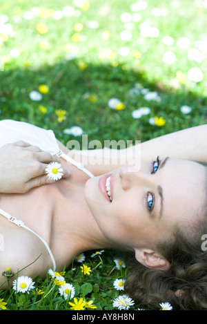 Junge Frau im Grass liegen, die Blume, lächelnd in die Kamera Stockfoto