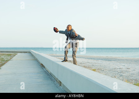 Geschäftsmann stehend auf Mäuerchen am Strand, Arme, halten Fußball Stockfoto