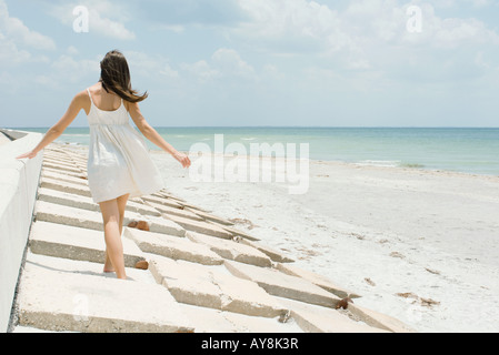 Junge Frau zu Fuß entlang der niedrigen Mauer am Strand, Rückansicht Stockfoto