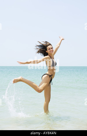 Junge Frau am Strand sprang, ein Bein, hob die Arme Stockfoto