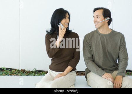 Paar, sitzen, Mann tragen Kopfhörer lächelnd an einander, Frau mit Handy, Stockfoto