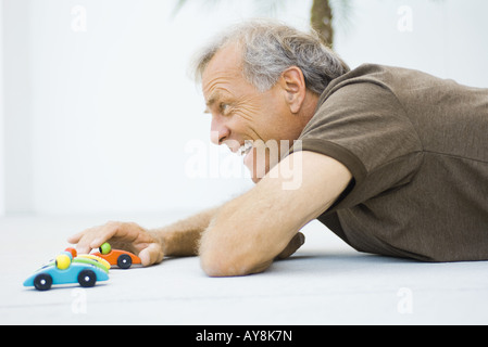 Reifer Mann auf dem Boden, spielen mit Spielzeug-Autos, lächelnd, Seitenansicht Stockfoto