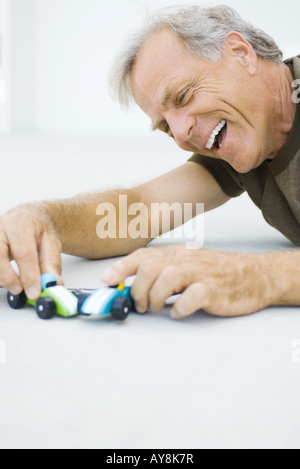 Reifer Mann auf dem Boden, spielen mit Spielzeug-Autos, lächelnd, Nahaufnahme Stockfoto