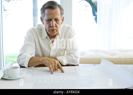 Mann, Studium der Baupläne im Hause, Tasse Kaffee in der Nähe Stockfoto