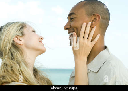 Paar lächelnd an einander, zarte Frauenhand auf Mannes Wange, Seitenansicht Stockfoto