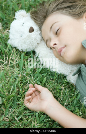 Junge im Grass liegen mit geschlossenen Augen, Kopf ruht auf Teddybär Stockfoto