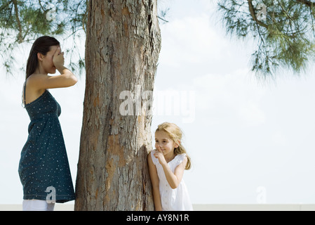 Zwei Schwestern Versteckspiel, eins für Augen mit den Händen, spähen der andere um Baumstamm Stockfoto