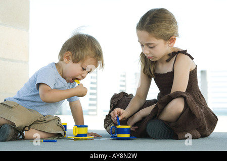 Bruder und Schwester sitzen auf dem Boden, mit Kunststoff Teetassen zusammen spielen Stockfoto