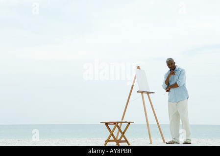 Senior woman stehen neben leeren Leinwand am Strand, mit Pinsel, lächelnd in die Kamera Stockfoto