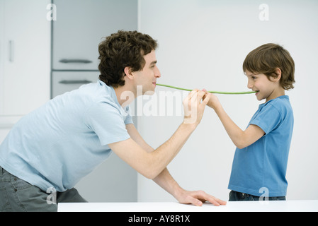 Vater und Sohn von Angesicht zu Angesicht stehen grüne Bohnen zwischen ihren Mündern hochhalten Seitenansicht Stockfoto