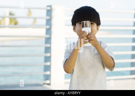 Kleiner Junge hält Dia-Kamera-Handy vor Gesicht, Vorderansicht Stockfoto