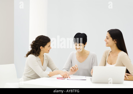 Drei Geschäftsfrauen sitzen am Tisch, diskutieren Dokument, Lächeln Stockfoto