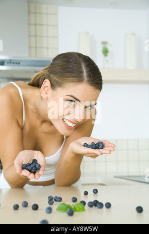 Frau in Küche, hält eine Handvoll Blaubeeren, lächelnd in die Kamera Stockfoto