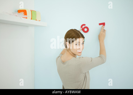 Vermittlung von dekorativen Zahlen auf Wand, über die Schulter in die Kamera lächelnde Frau Stockfoto