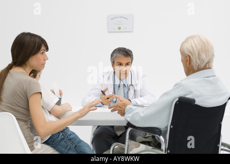 Arzt am Schreibtisch, Gespräch mit älteren Patienten und seine Familie Stockfoto