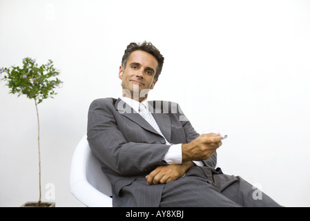 Geschäftsmann, sitzen, anhören von MP3-Player, lächelnd in die Kamera Stockfoto