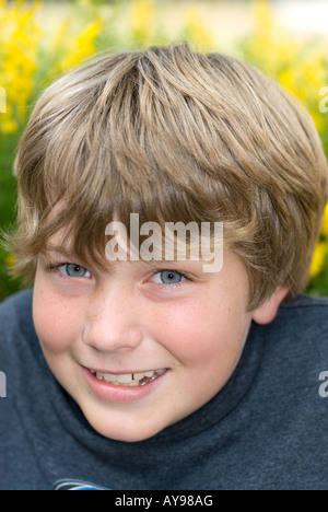 Ein 9-jähriger Junge lächelt beim Ausruhen in einem Feld von gelben Sprintime Blumen Stockfoto