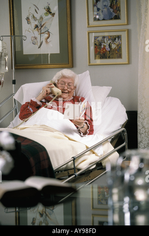Kranke weiblichen senior Patienten im Bett liegend betrachten bekommen gut Karte und Gespräch am Telefon Stockfoto