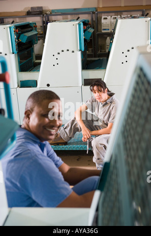 Porträt eines Mannes und einer Frau in Overalls hinter einer Druckmaschine Stockfoto