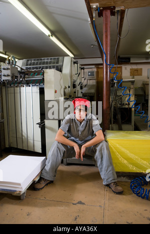 Porträt einer Frau in Overalls sitzt neben einigen Maschinen Stockfoto