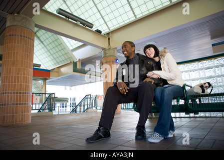 Inter-racial Pärchen sitzen auf einer Bank an einem öffentlichen Bahnhof Stockfoto