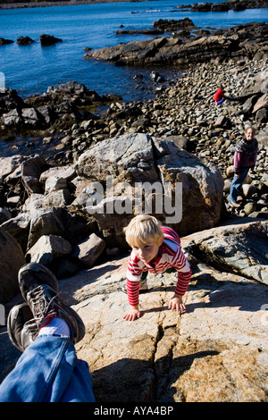 Ein Junge (4 Jahre) klettert einen Felsen (wie Mutter blickt auf) an der Küste in Biddeford, Maine. Holz-Punkt. Stockfoto