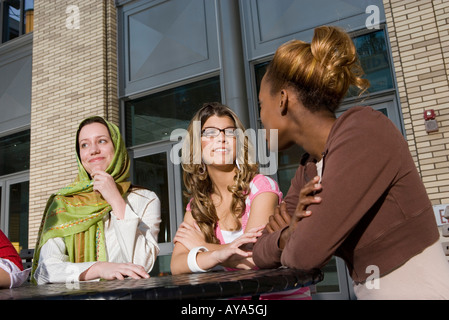Drei junge Frauen sitzen an einem Tisch außerhalb eines Gebäudes, Geselligkeit und im Gespräch Stockfoto