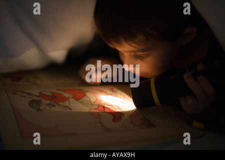 Lesen unter der Bettdecke bei Fackelschein Stockfoto