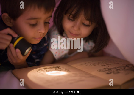 Lesen unter der Bettdecke von Torchlight Mädchen im Alter von vier Jahren sechs jungen im Alter von Stockfoto