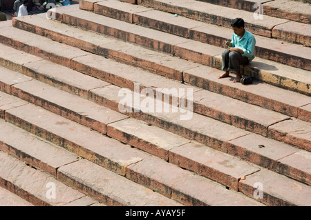 Junger Mann saß auf den Stufen der Jama Masjid Moschee in Alt-Delhi, Indien. Er hat sich die Schuhe ausgezogen, möglicherweise im Begriff, zum Freitagsgebet hineinzugehen. Stockfoto