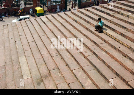 Junger Mann saß auf den Stufen der Jama Masjid Moschee in Alt-Delhi, Indien. Er hat sich die Schuhe ausgezogen, möglicherweise im Begriff, zum Freitagsgebet hineinzugehen. Stockfoto