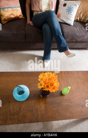 Erhöhten Blick auf Blumen in einer Vase auf Couchtisch mit Frauenbeine auf Sofa im Hintergrund Stockfoto
