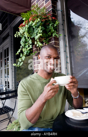 Porträt eines lachenden jungen Mannes hält eine Kaffeetasse in einem Straßencafé Stockfoto