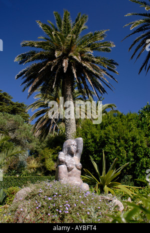Statue von Gaia Mutter Erde unter einer Palme an einem hellen Sommertag mit blauem Himmel in Tresco Abbey Gardens Stockfoto