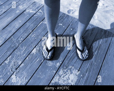 Frau die Füße in Flip Flop Sandalen auf Boardwalk am Strand Stockfoto