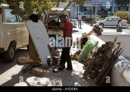 Mann, der mit geschnitzten Skulpturen und anderen zum Verkauf stehenden Gegenständen auf dem afrikanischen Fluchtmarkt in Stellenbosch, Westkaps, Südafrika steht Stockfoto