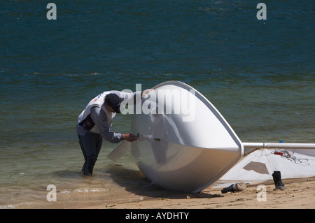 Man prüft den Rumpf seine Jolle am Ufer, Pittwater, Sydney, Australien Stockfoto