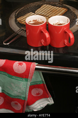 Toasten von Brot auf der Heizplatte ein Aga mit zwei roten Becher heiße Getränke warm zu halten, an der Spitze Stockfoto