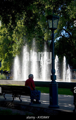 Mann sitzt auf einer Parkbank vor eine Wasserfontäne im Plaza Independencia in Mendoza Argentinien Stockfoto