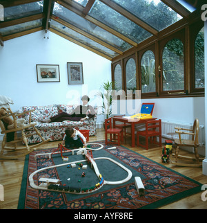 Mutter liegen auf Sofa und Kind spielt mit Spielzeugeisenbahn im Wintergarten-Erweiterung Stockfoto