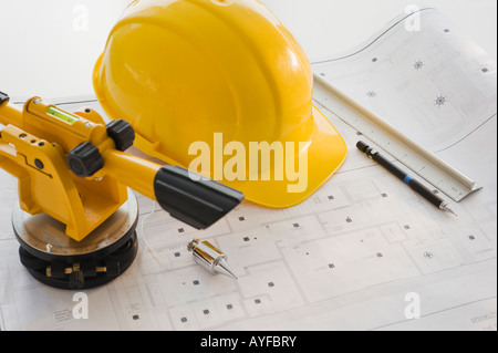 Schutzhelm und Vermessungsgeräte auf Blaupausen Stockfoto