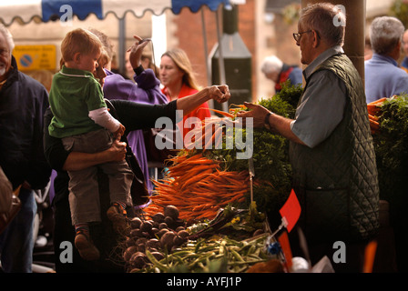 EIN SHOPPER KAUFEN EIN PAAR KAROTTEN MIT IHREM KIND AUF DEM BAUERNMARKT IN STROUD GLOUCESTERSHIRE UK Stockfoto