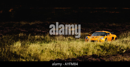 Panoramablick auf ein oranges Lotus Exige Auto, das durch die North Yorkshire Moors, Großbritannien gefahren wird. Stockfoto