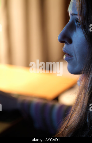 Frau sitzt hinter einem Schreibtisch mit ihrem Gesicht beleuchtet von einem Computer-Monitor, Close Up. Stockfoto