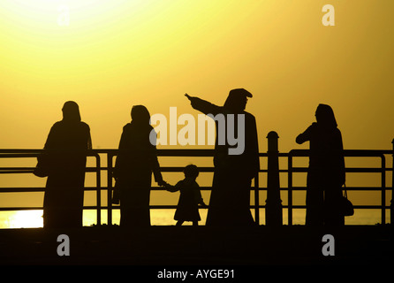 Kuwaitis in traditioneller Kleidung spazieren das Dock an der Uferpromenade der Sonnenuntergang über dem Persischen Golf Stockfoto